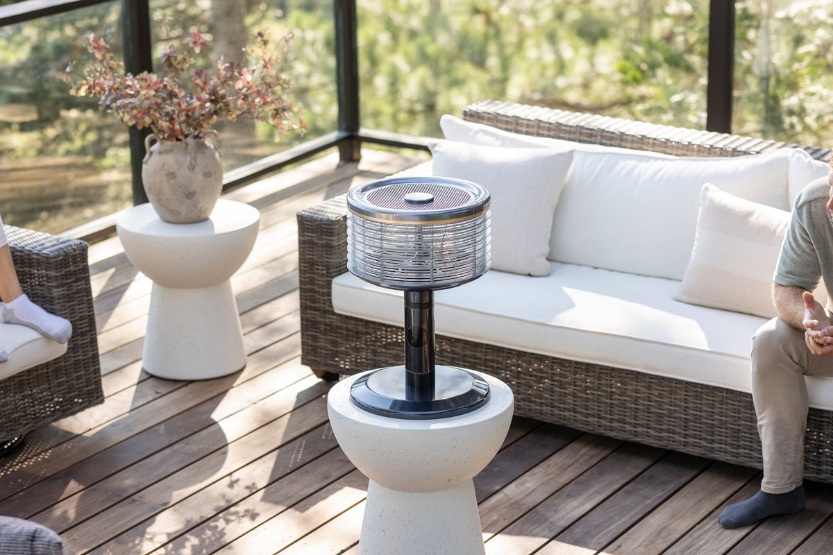 Ventilador Orbi360 negro sobre una mesa auxiliar en una terraza con sofá de mimbre