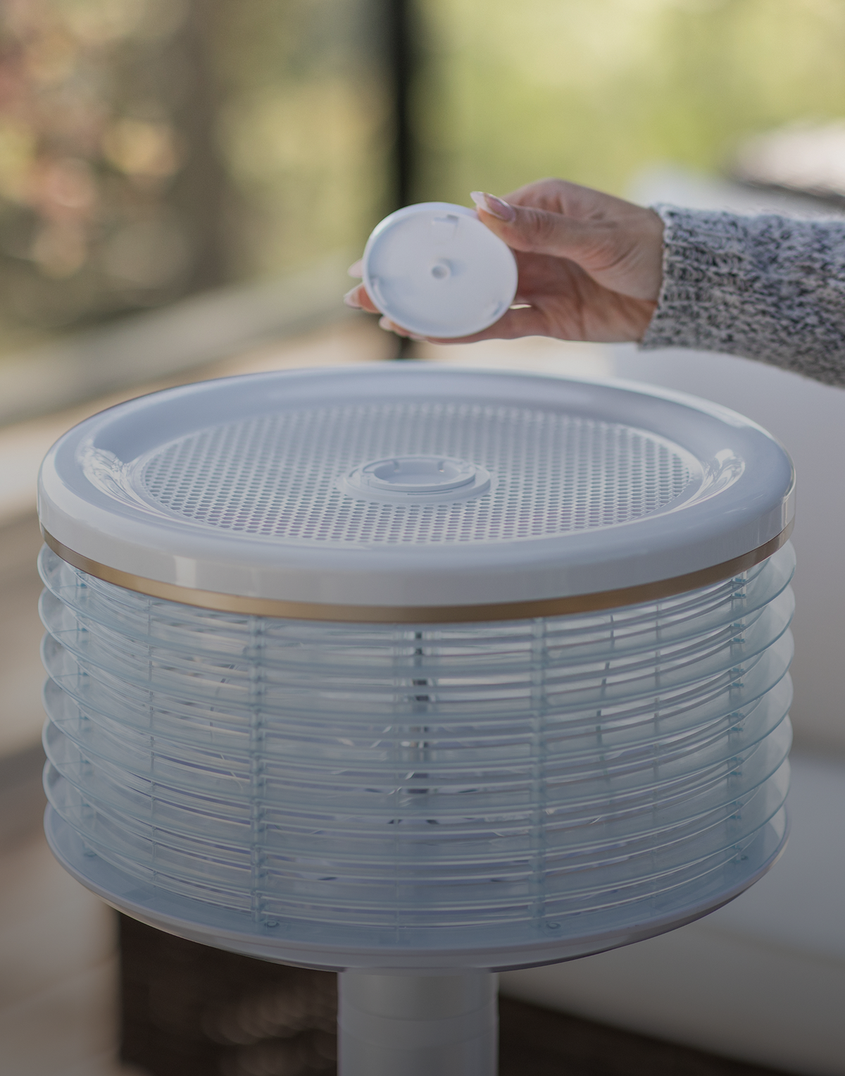 Mano colocando una cápsula aromática sobre la rejilla superior del ventilador Orbi360 blanco